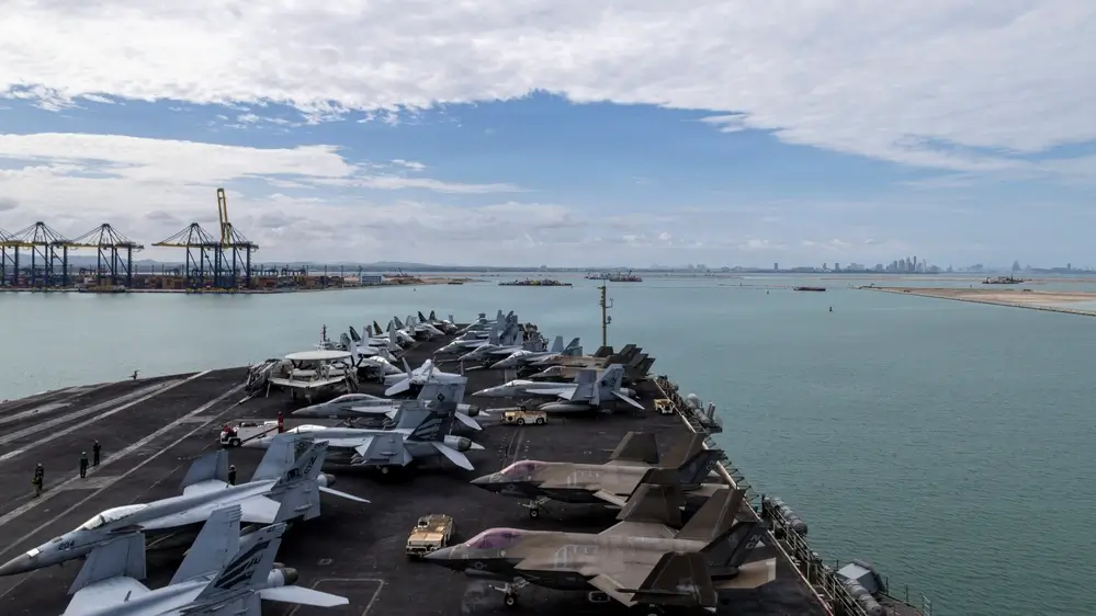The supercarrier USS Abraham Lincoln docked in Thailand, showing heavy streaks of running rust and algae along the waterline and sponsons.